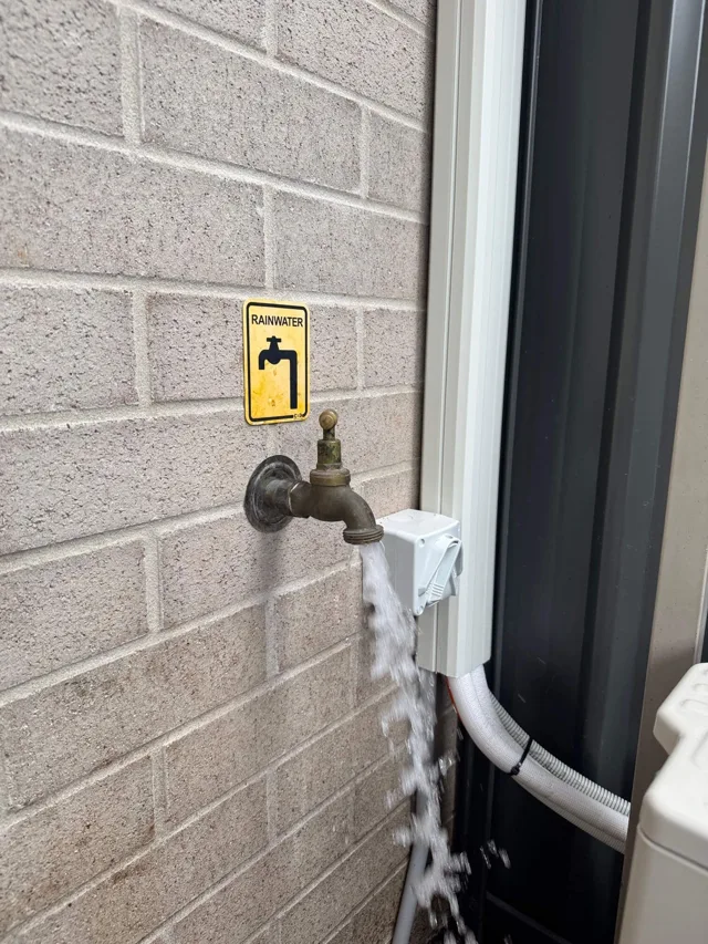 Rainwater tap and pipework beside a tank at a house