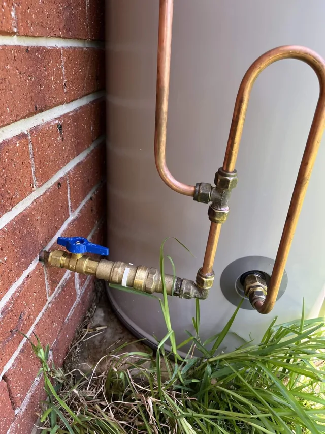 Hot water unit with copper pipework and valves beside a brick wall